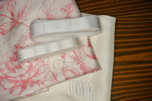 The Pink Floral Satin Jet Set Kit features a pink floral pattern on ivory satin fabric and a solid ivory satin fabric; white elastic; and white rings, g hooks, and sliders.